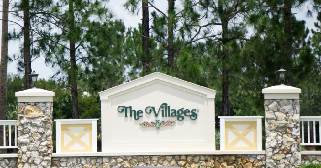 The Villages, Florida/USA - June 2, 2020 - The Villages entrance sign, a retirement community, surrounded by colorful flowers, brick pillars and pine trees on a sunny summer day.