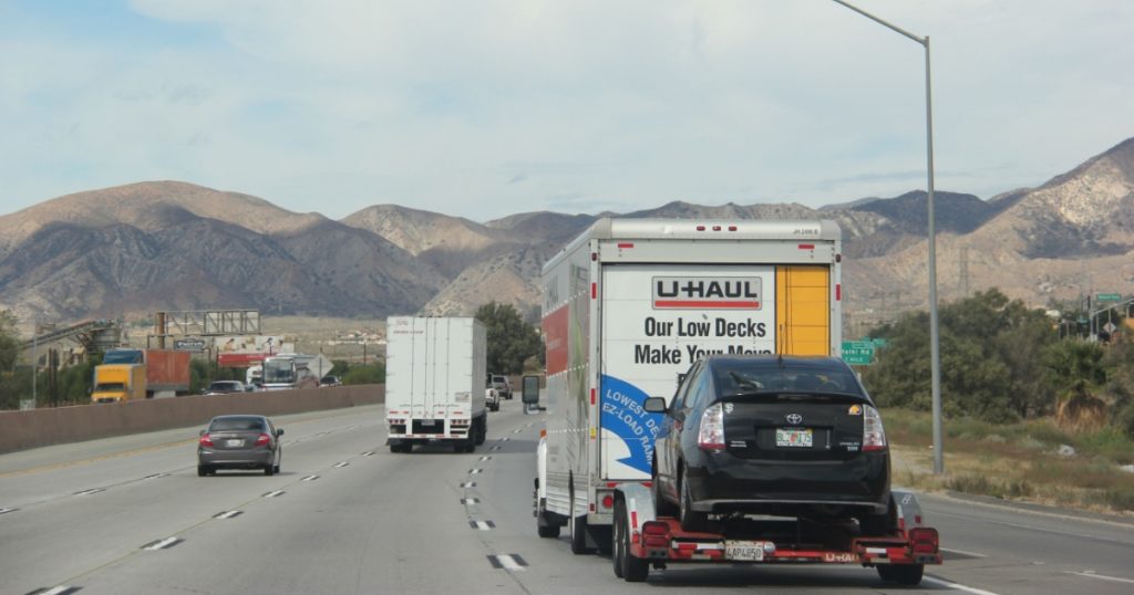 U-Haul Truck is towing a car on a freeway. U-Haul, an American moving equipment and storage rental company, provides trucks for rental suitable for moving.