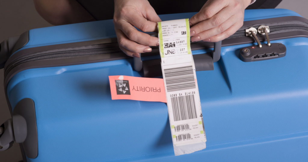 Airline check in luggage tag being attached to a suitcase. Priority tags