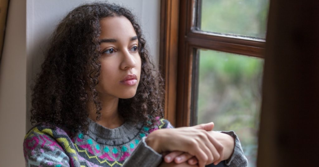 Beautiful mixed race biracial African American girl teenager female young woman sad depressed or thoughtful looking out of a window