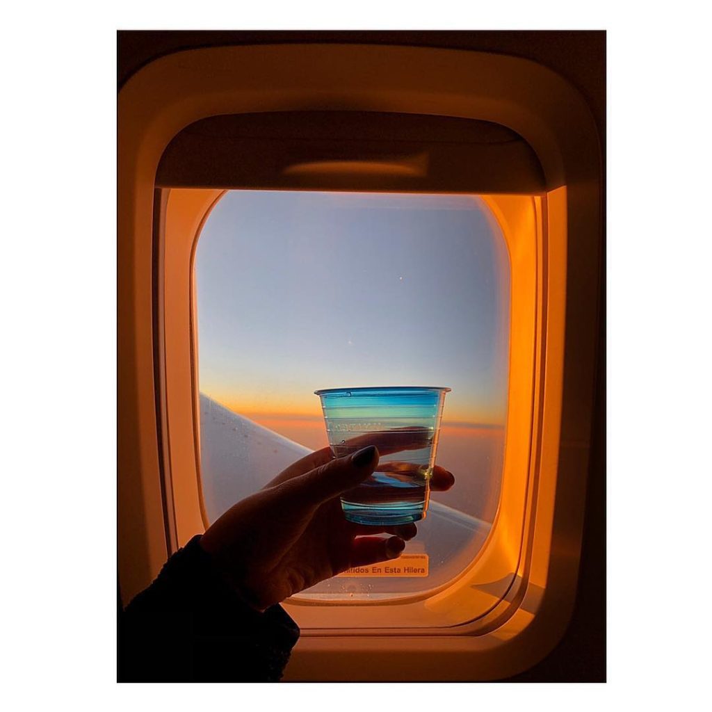 Hand holding a cup in front of airplane window. 