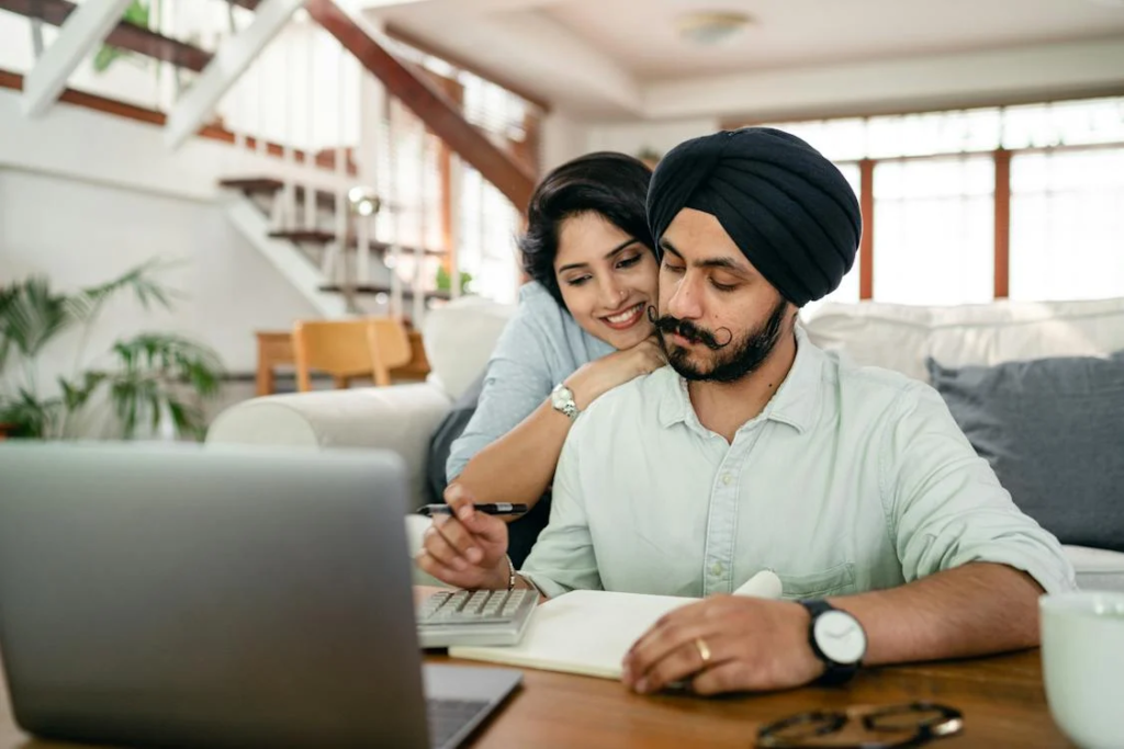 stay-at-home jobs - Serious young Sikh man with hugging wife counting on calculator at home
