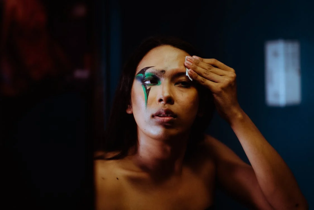 Androgynous ethnic woman removing dark body art on face
