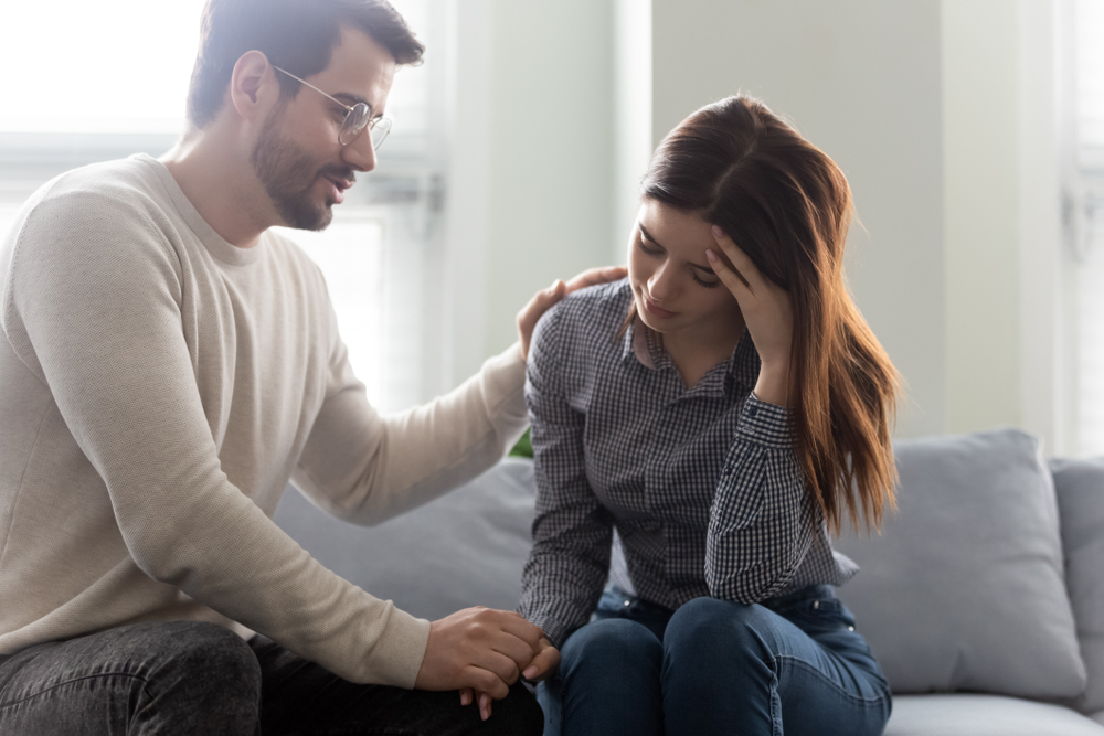 Unhappy stressed woman sitting on sofa with empathic husband. Caring man comforting desperate wife, demonstrating support and love, giving psychological help, overcoming personal problems together.