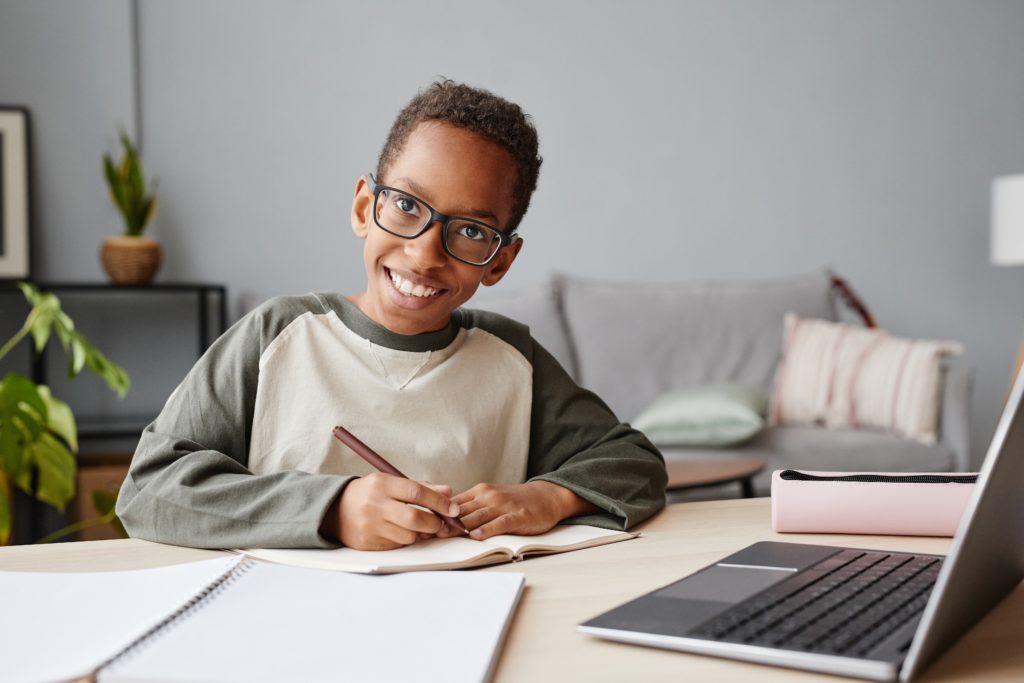 Portrait of smiling African-American boy wearing glasses while studying at home, homeschooling concept, copy space
