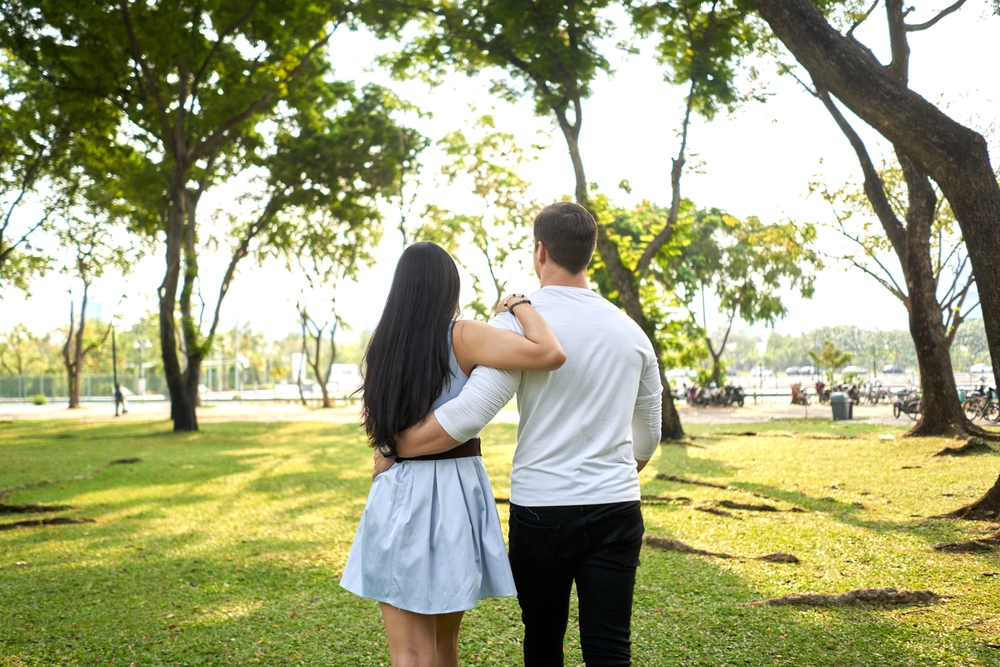Back of multiracial couple walking in an urban park holding each other's backs