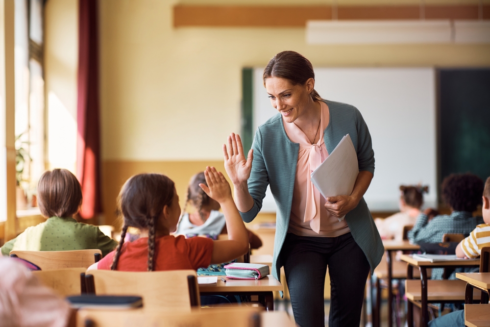 Happy elementary school teacher giving high-five to her student during class in the classroom.
