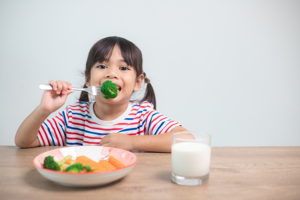 Cute asian child girl eating healthy vegetables and milk for her meal
