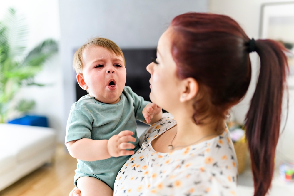A mother holding child baby on the living room. The baby is sick having some cough
