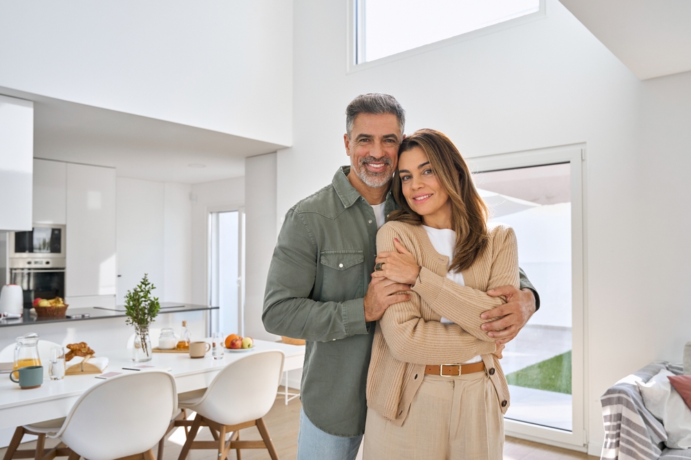 Happy smiling middle aged romantic affectionate couple mature older man and woman hugging standing at home together looking at camera enjoying bonding in modern house living room. Portrait.