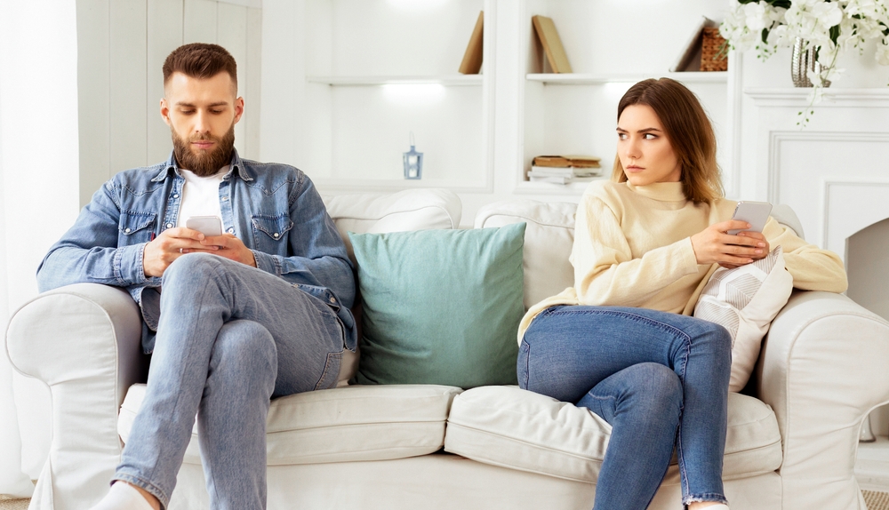 Couple Crisis. Man Using Phone, Not Paying Attention To Wife, Sitting On Couch