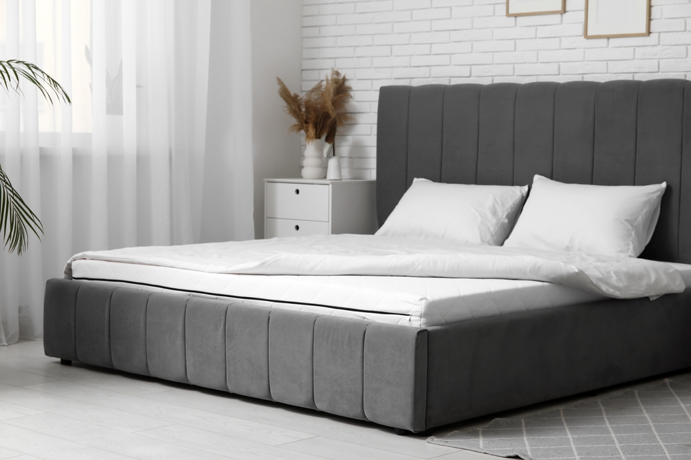 New orthopedic mattress with blanket on stylish bed in room