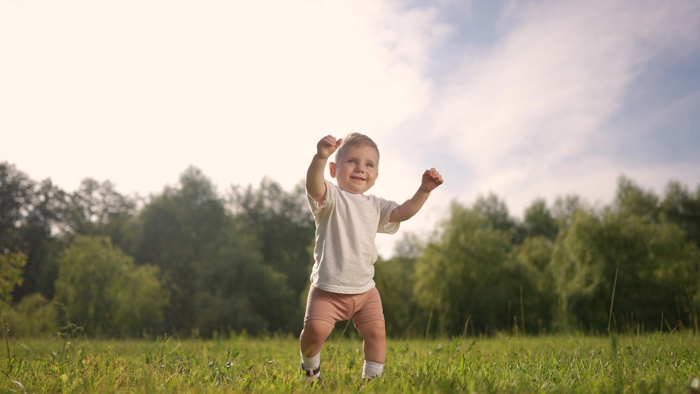 A baby is taking the first steps in a park. Child toddler happy family step concept. Baby steps on the grass in nature. Baby taking first steps on grass park. lifestyle family motherhood concept.
