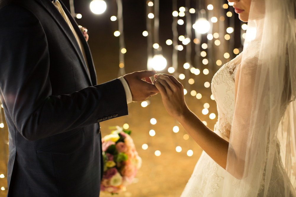 Evening wedding ceremony. The bride and groom holding hands on a background of lights and lanterns.