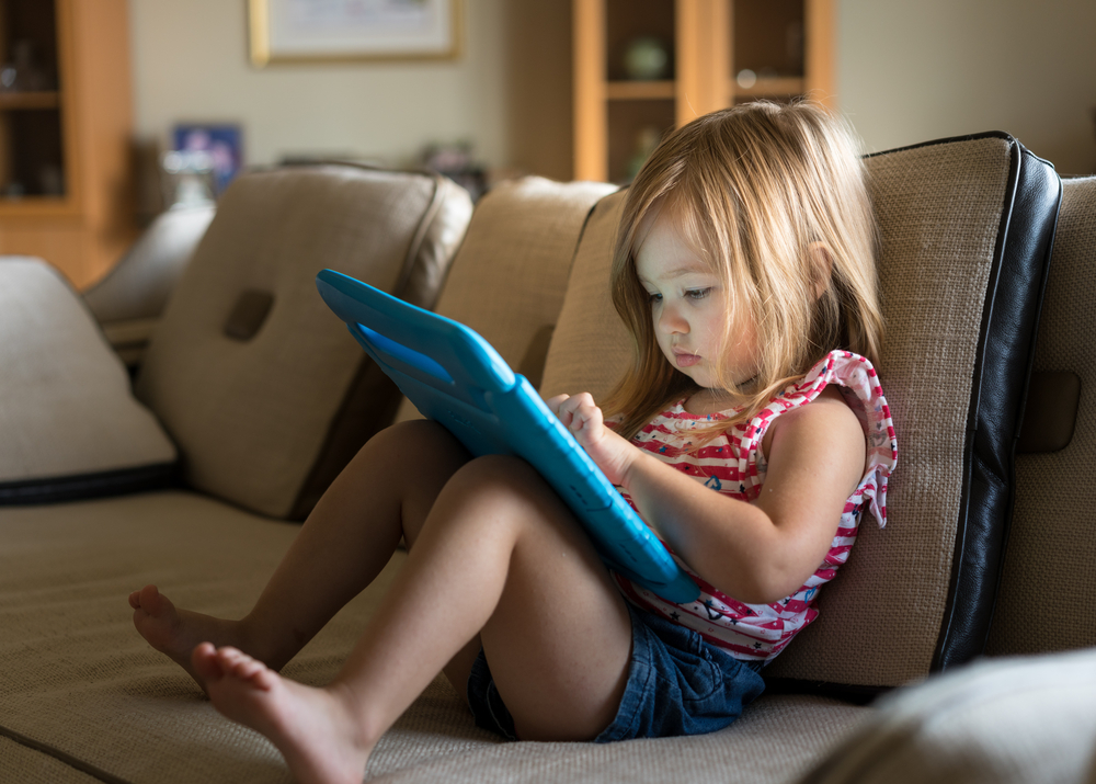 Young girl sitting at home on settee and using a child's tablet touch screen computer
