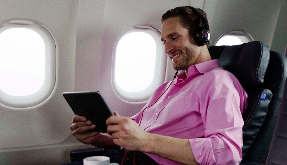 Man smiling and looking at iPad with headphones. Airplane windows in the background.