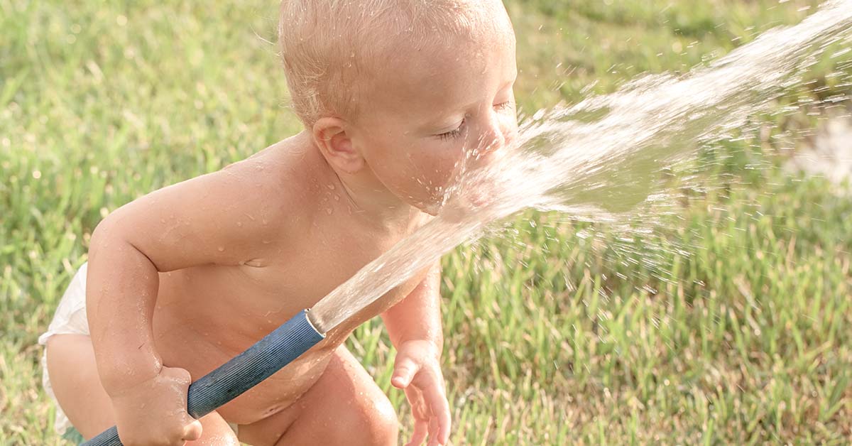 child drinking water from garden hose