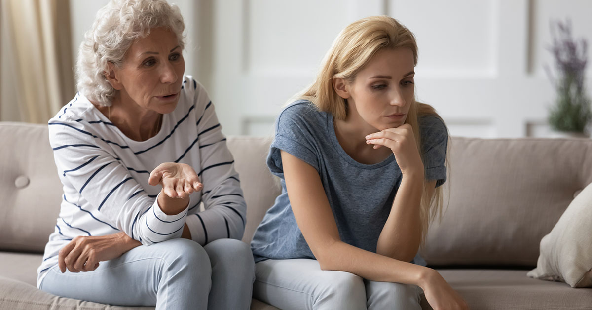 elderly mother and adult daughter sitting on couch together in dispute