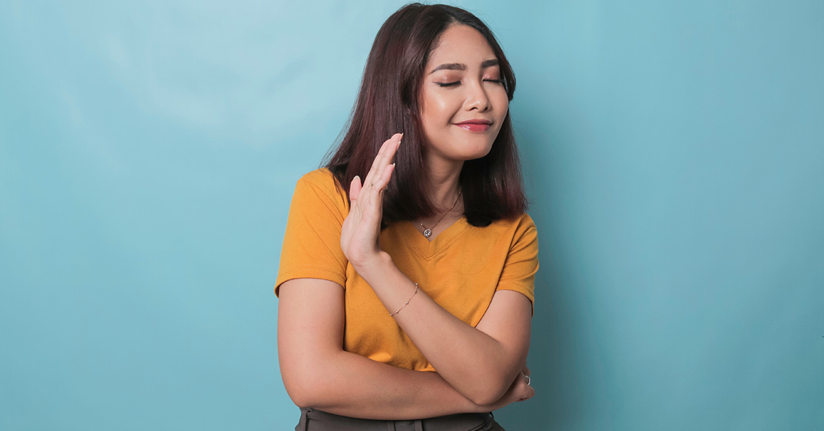 woman in orange shirt standing in front of a blue background with her hand up