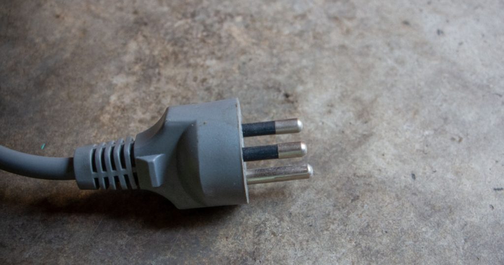 Closeup photo of the third prong power plug or electrical plug on the cement floor.