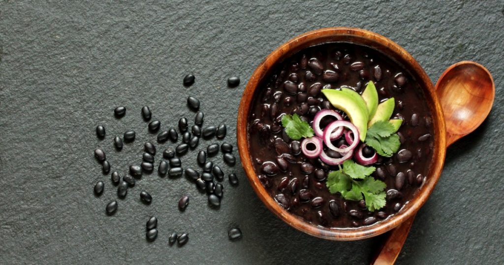 black bean soup or stew. Latin American or Mexican cuisine. stewed black beans served with avocado and red onion and cilantro. place for text. top view.