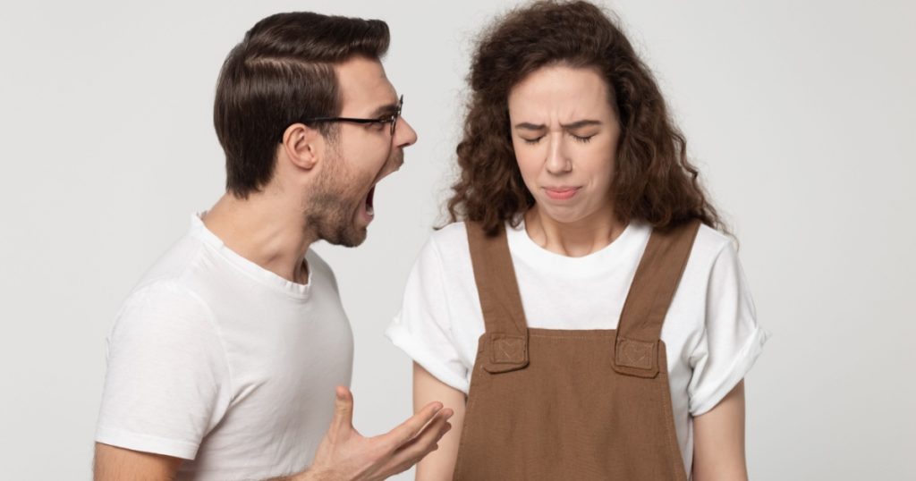 Young unhappy couple isolated on grey studio background, mad angry guy open mouth screaming at girlfriend, girl standing desperate listening aloud yelling feels weak abused crying unable to fight