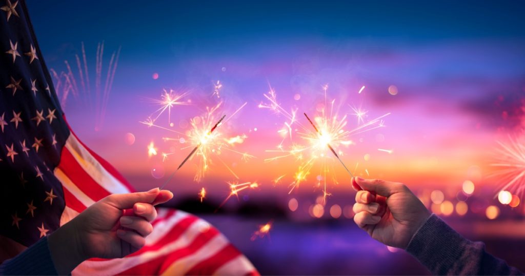 Usa Celebration With Hands Holding Sparklers And American Flag At Sunset With Fireworks