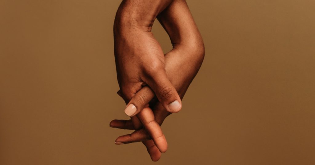 Couple standing side by side and holding hand with interlocked fingers. Cropped shot of two hands together showing unity.