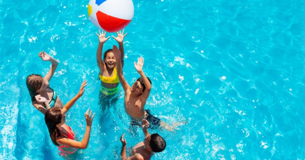 Group of kids in swimming pool play with inflatable ball view from above reaching hands up