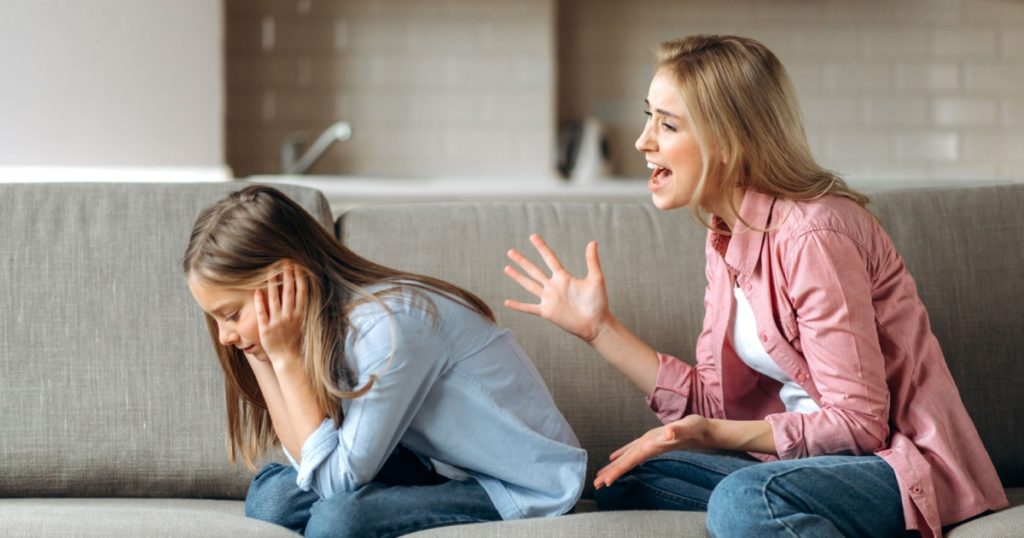 Conflict of mom and daughter. Screaming mother, shouts at little daughter scolding her. Little girl is ignoring mom, close her ears with arms. Complicated relationships of mother and child