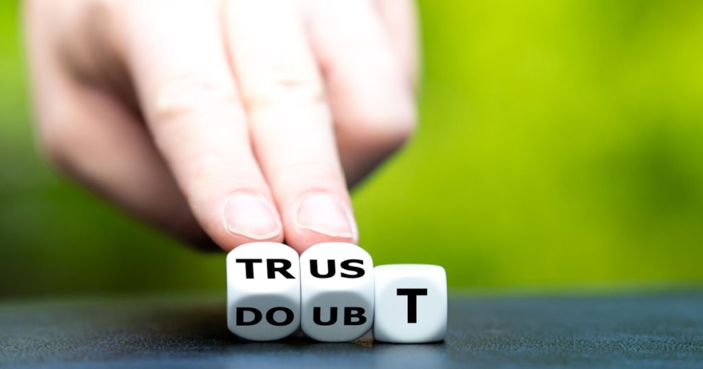 Hand turns dice and changes the word doubt to trust.