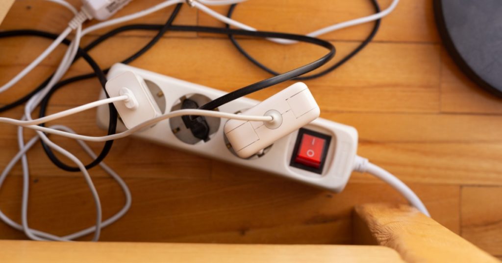Multiple chargers with messy cords plugged to a single extension strip on wooden parquet floor