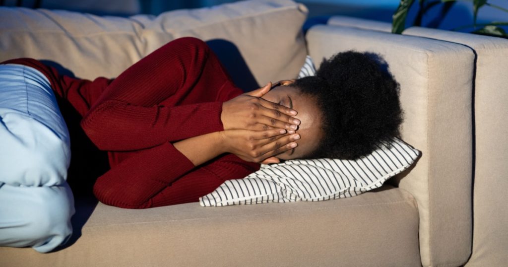 Frustrated upset african woman lying on couch and crying, covering face with hands, worrying about personal problems or troubles at work. depressed black female feeling persistent sadness and anxious