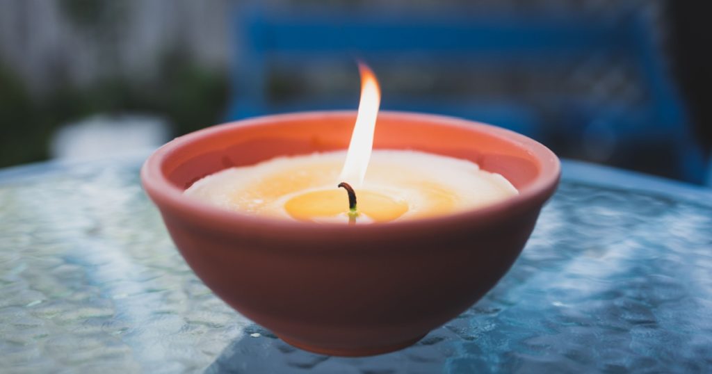citronella candle with flame outdoor on cafe table setting at dusk for protection against mosquitoes during summer nights
