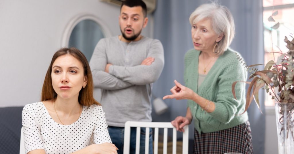 Woman ignoring her husband and mother-in-law standing behind and arguing with her at home.