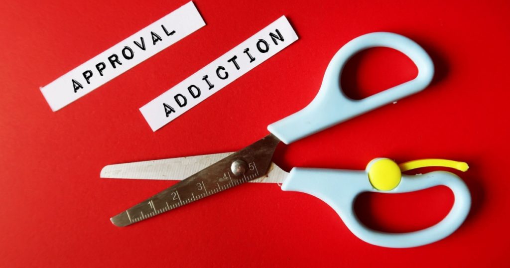 Scissors on blue background with text written paper pieces APPROVAL ADDICTION, refers to feeling insecure and unworthy of validation seeker, addicted to approval and validation from others