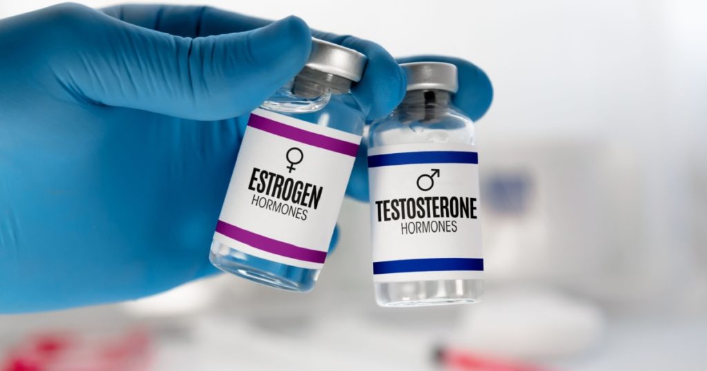 Hand of doctor with two injection vials for treatment with Testosterone and Estrogen hormones. Doctor With bottles for Testosterone and Estrogen hormonal balance therapy