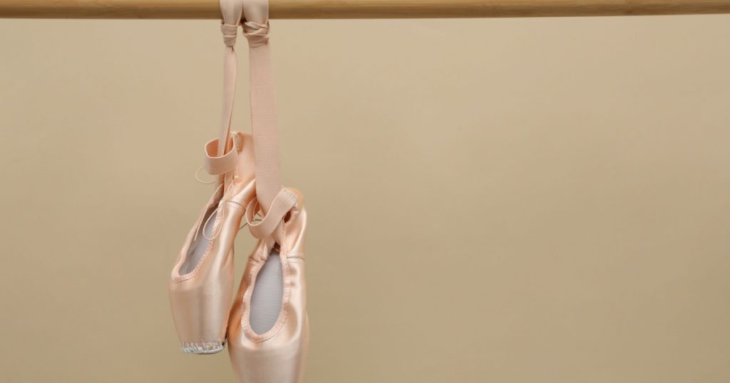Elegant pointes hanging on ballet barre against beige background. Space for text