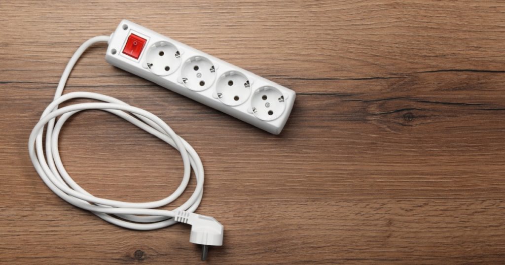 Power strip with extension cord on wooden floor, top view. Space for text

