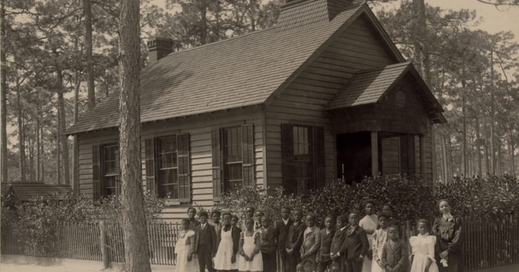 African American school children posed with their teacher outside a segregated one-room school, in South Carolina. Ca. 1905
