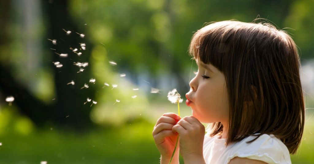 Beautiful child with dandelion flower in spring park. Happy kid having fun outdoors.