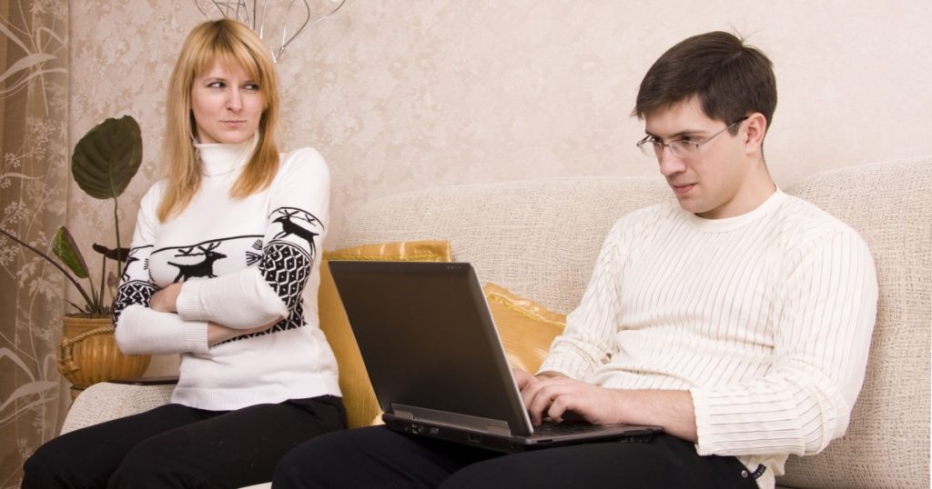 Woman is angry with man for working at laptop. Female takes offence at male. Man is sitting on the sofa and he is busy.