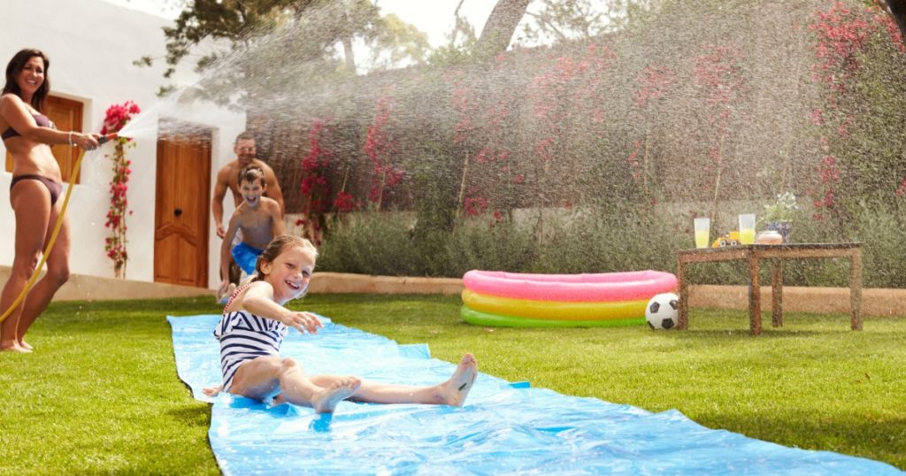 Family Having Fun On Water Slide In Garden