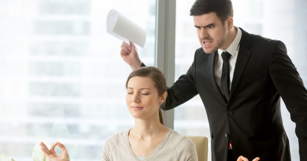 Calm attractive businesswoman practicing yoga at work, meditating in office with eyes closed, ignoring angry bad boss standing behind her back, avoiding negative people, positive thinking, no stress
