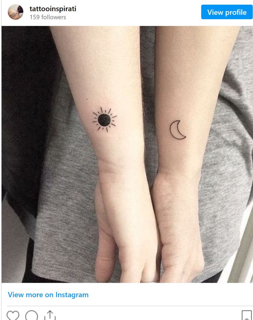 Arms with moon and sun tattoos. Gray shirt in the background. 