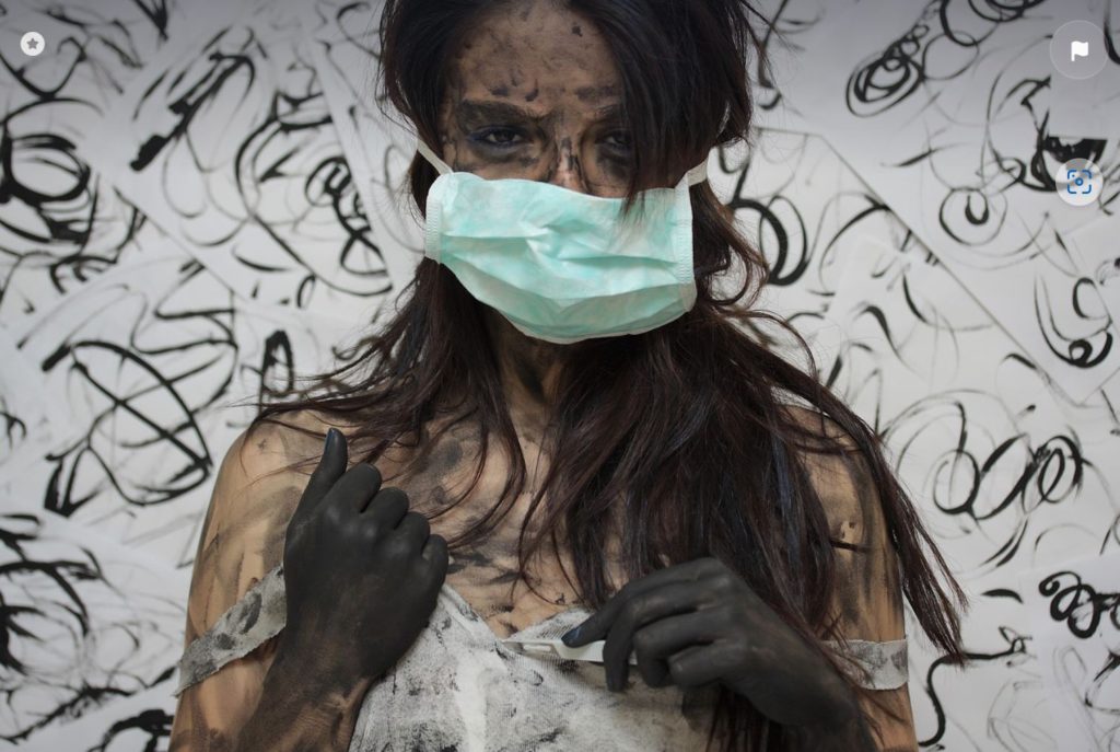 Woman wearing mask, covered in paint. Black and white background.