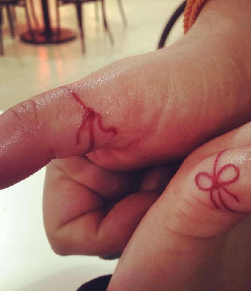 Couple's tattoo with red string on hands. Table, chairs, and white floor in the background. 