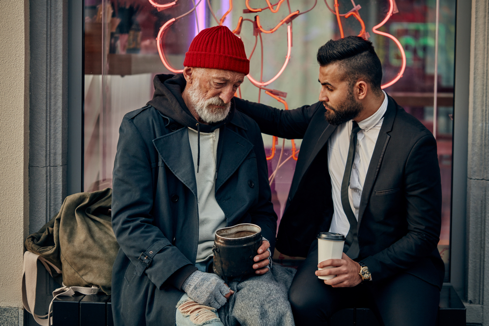 Rich man in tuxedo and homeless person in dirty clothes sitting and talking in the street. Poverty, help