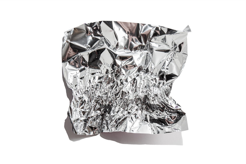 White shiny aluminum foil wrap without chocolate candy on a white background. Texture of used crumpled aluminium food foil.