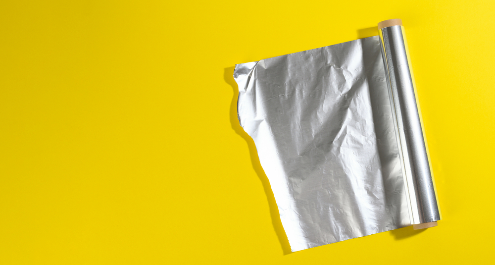 Roll of twisted food foil for packaging food on yellow background, top view